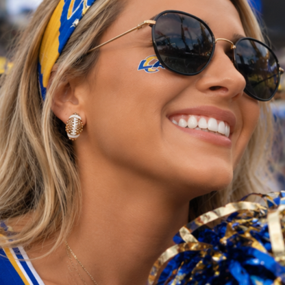 Woman wearing sunglasses and a headband with a logo, smiling. Rhinestone football earring studs soberafshop
