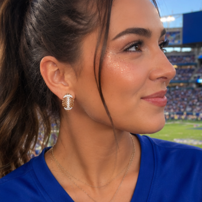 Woman wearing gold earrings with a stadium in the background with football rhinestone stud earrings