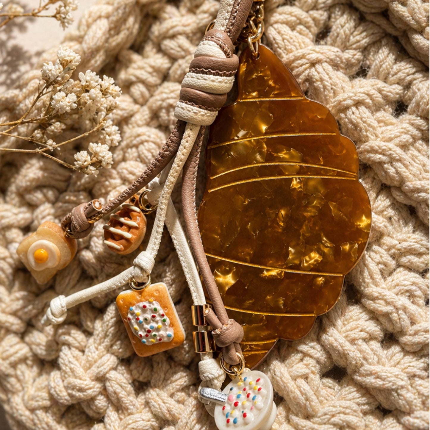 Decorative keychain with leaf and small charms on a textured beige surface criossant. Breakfast charms