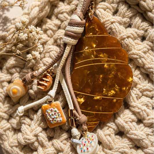 Decorative keychain with leaf and small charms on a textured beige surface criossant. Breakfast charms