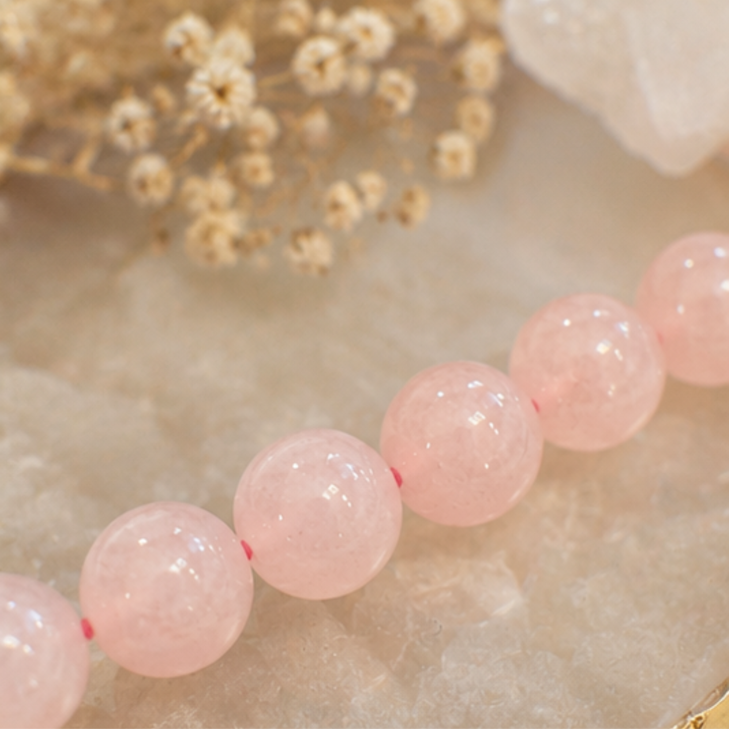 Close-up of pink quartz beads on a textured surface with dried flowers in the background