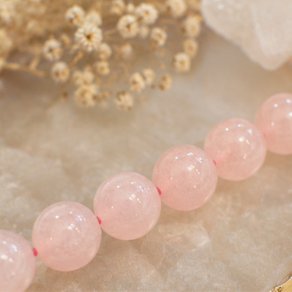 Close-up of pink quartz beads on a textured surface with dried flowers in the background